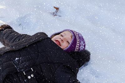 High angle view of girl looking away while lying in snow during winter