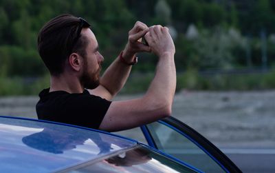 Side view of man photographing by car