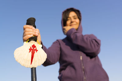 Low angle view of female hiker holding hiking pole while standing against clear sky