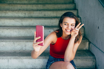 Portrait of smiling young woman using mobile phone while sitting on staircase