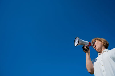 Low angle view of woman talking on megaphone against sky