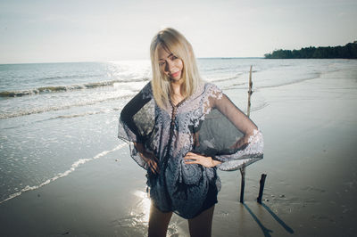 Young woman standing at beach against sky