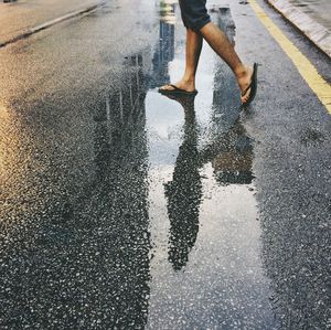 Low section of man with umbrella walking on wet road