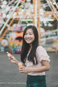 Smiling young woman holding bubble wand at amusement park