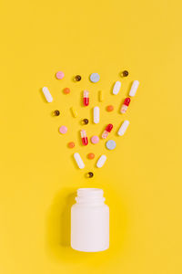 Directly above shot of pills spilling from bottle against yellow background