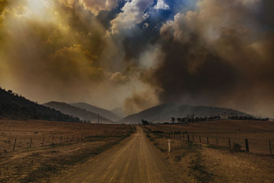 Dirt road amidst field against sky