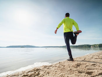 Legs stretching sportsman. adult man in yellow black training suit leisure on the sandy beach.