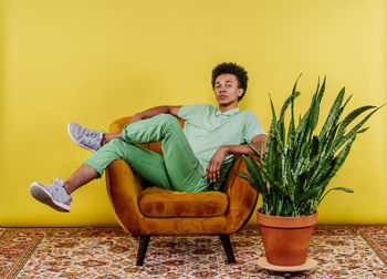 Young man sitting on chair against yellow wall