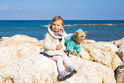 Full length of happy boy on rock at beach against sky