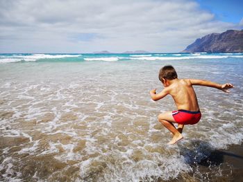 Full length of shirtless boy on beach against sky