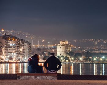 Rear view of people looking at illuminated buildings against sky