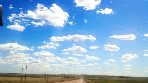 Road passing through field against cloudy sky