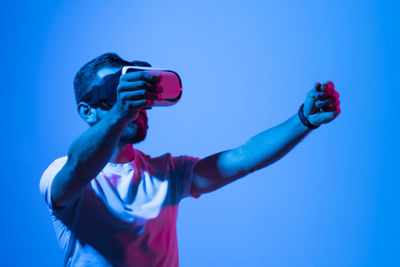 Side view of young man photographing against blue background