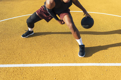 Diligent mixed race african american sportsman in uniform concentrating on dribbling ball and kicking goal on yellow playground