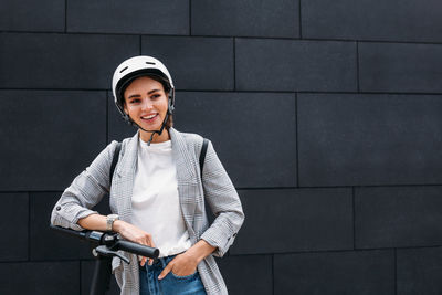 Portrait of smiling young woman standing against wall