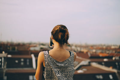 Rear view of woman photographing city while standing on terrace against sky