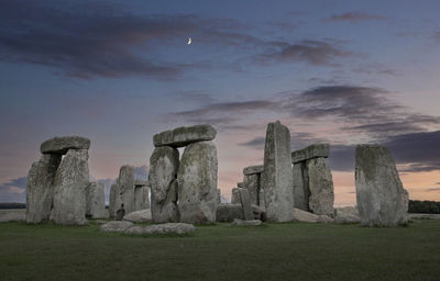 Dolmen at stonehenge in twilight with moon at sunset.