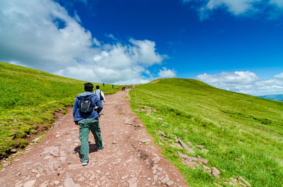 Rear view of man walking on grass against sky