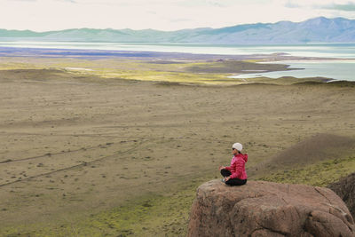 Rear view of man sitting on sand at desert