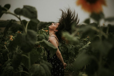 Side view of young woman tossing hair while at sunflower farm