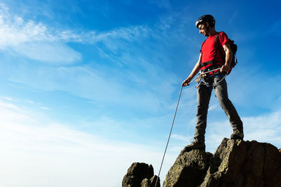 Low angle view of man climbing on rock against sky