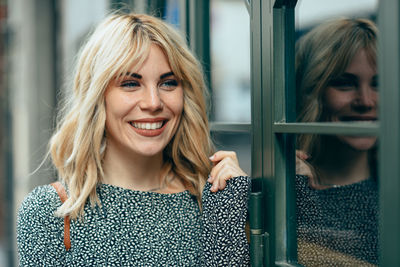 Smiling young woman looking away while standing by store window