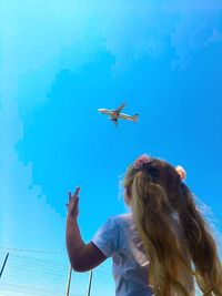 Rear view of woman with airplane flying against blue sky