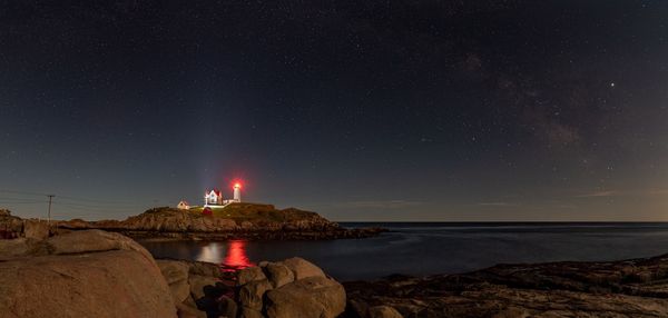 Lighthouse by sea against sky at night