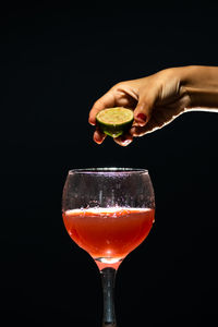 A hand holding a slice of lemon above a glass goblet with guava juice inside. 