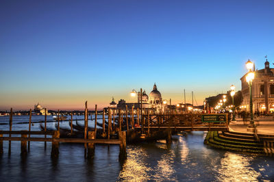 Boats moored in illuminated city against clear sky