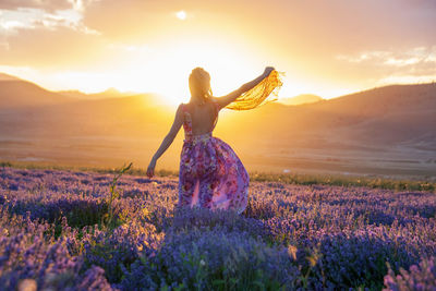 Rear view of woman standing on field against sky during sunset