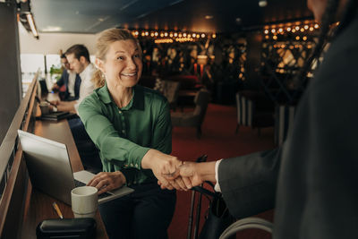 Smiling mature businesswoman handshaking with colleague in hotel lounge