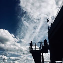 Low angle view of silhouette man standing on railing against sky