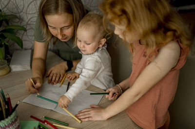 Mother and daughters drawing together with color pencils at home