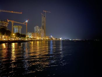Illuminated buildings by river against sky at night