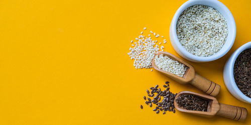 Wooden spoons with sesame and flax seeds lies in a white mortar on a yellow background. healthy eat