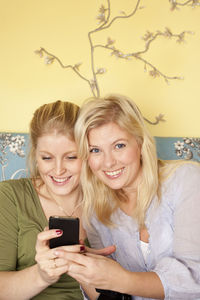 Two young women using mobile phone in bedroom