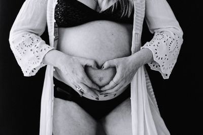 Midsection of woman touching face against black background