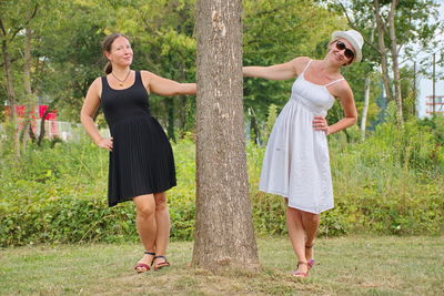 Portrait of women standing by tree trunk in park
