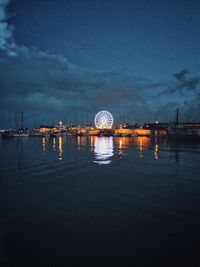 Illuminated ferris wheel by sea against sky at night