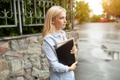 Woman holding book while standing outdoors
