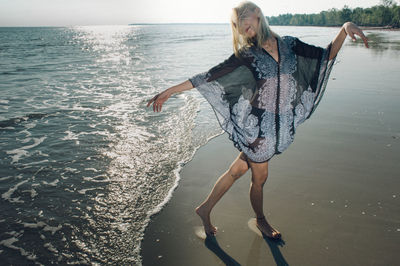 Portrait of playful woman with arms outstretched standing at beach