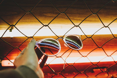 Close-up of hand against chainlink fence