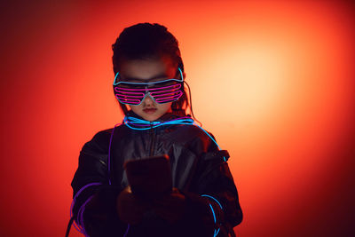 Portrait of robot boy child from the future in neon glasses and jacket looking at the phone at night