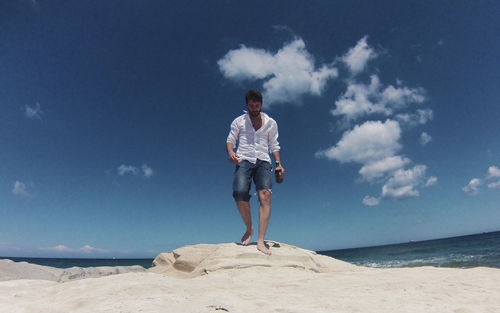 Full length of young man walking at beach against sky during sunny day