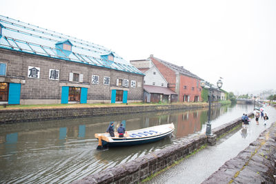 Boats in river by buildings against clear sky