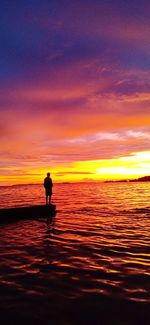 Silhouette person standing on sea against orange sky