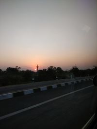 Road by silhouette trees against sky during sunset