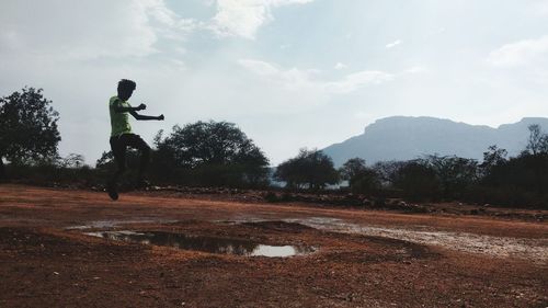 Man jumping over landscape against sky