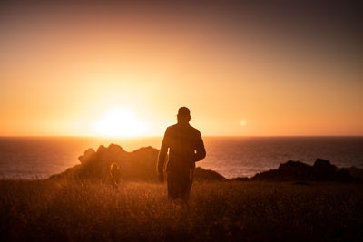 Silhouette man and woman standing against sea and sky during sunset